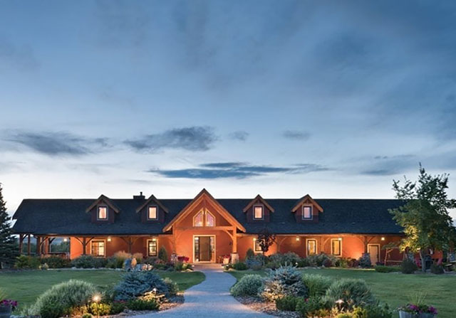 one story timber frame home with all the lights on at dusk