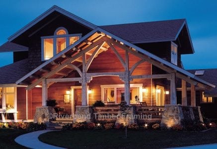 timber frame home with a large outdoor timber frame entrance at night with the lights on