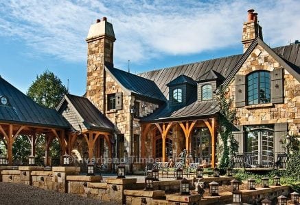 timber frame home with multi colored tan stone exterior with outdoor timber frame area with a lake in the background