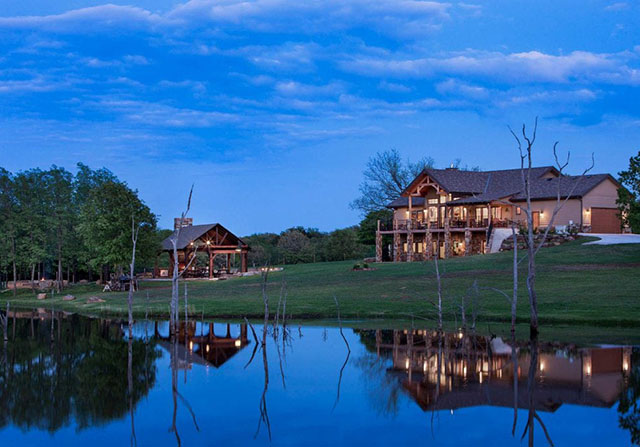 timber frame home with a lake in the front yard at dusk