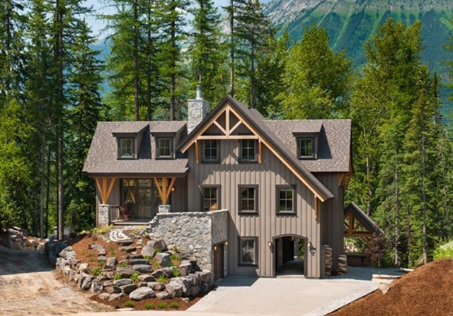 grey timber frame home with dense forest behind that leads up a mountain side